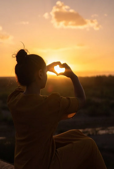 Une femme fait un cœur avec ses mains face au coucher de soleil, symbole de l'ambiance chaleureuse de Mass'Mie à Auterive.